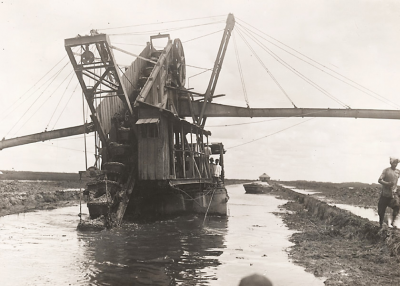 A steam dredge on a smaller canal. The wings are conveyors to bring the sediments aside and help build an embankment.